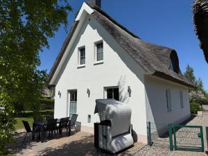 una casa bianca con il tetto di paglia e sedie nere di Reethaus Sonnenwiese, Haus am Meer mit eingezäuntem Garten, Hunde herzlich willkommen a Glowe
