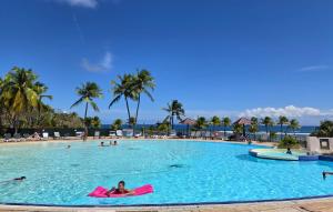 a woman laying in a large swimming pool at a resort at Studios Angoreva vue mer - côté plage ou jardin - Village vacances - Sainte-Anne Guadeloupe in Courcelles Sucrerie