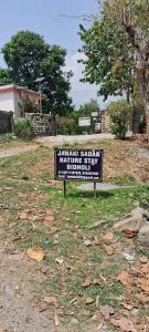 a sign sitting in the grass in a yard at Nature Stay-The Himalayan Foot Hills-JANAKI SADAN Two Bed Room Garden Home with attached bath room in each room and Kitchen with garden facing dinning space with Badminton Court in Mango Orchard in Jhājra