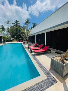 a swimming pool with red lounge chairs next to a building at Downwinder Lagoon Lodge in Kalpitiya