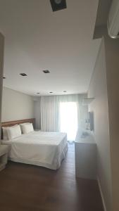 a white bedroom with a bed and a window at Apartamento TOP - No Praia Brava Hotel in Florianópolis