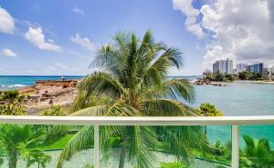 a view of the ocean and a palm tree on a balcony at Oceanview Sub Penthouse, Walk to Beach & Pool in San Juan