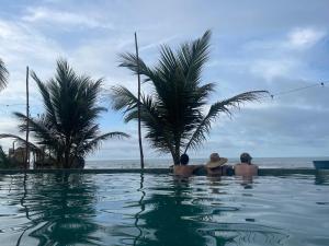 three people sitting in a swimming pool looking at the ocean at Cosamui Beach House in San Bernardo del Viento