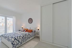 a white bedroom with a bed and a clock on the wall at Costa 27 Beach Apartment - By Y Concept in Costa da Caparica