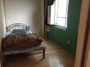 a bedroom with a bed with a green wall and a window at Asahi Guest House in Naha