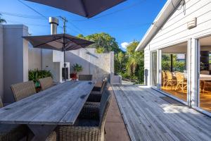 ein Holztisch im Freien mit Stühlen und einem Sonnenschirm in der Unterkunft Viletta Hauraki by Waiheke Pure in Waiheke Island