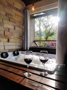two glasses of wine sitting on a table next to a bath tub at Estação 160 chalé Pico Agudo in Santo Antônio do Pinhal