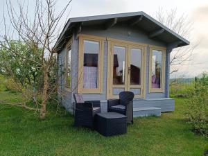 a small cabin with two chairs and a stool in the grass at Namelis Karklėje in Karklė