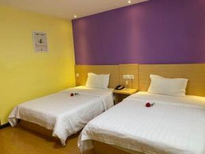 deux lits dans une chambre aux murs violets et jaunes dans l'établissement 7 Days Inn Huanggang Luotian Hedong Street Dabieshan Food Plaza, à Luotian