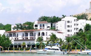 a large white building with a boat in the water at Hotel Marina Resort & Beach Club in Santa Cruz Huatulco