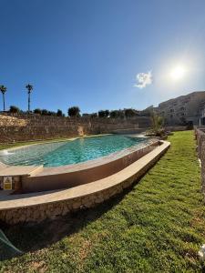 a swimming pool in a grassy field with the sun in the background at Hal Wardija Resort Apartments in Qala