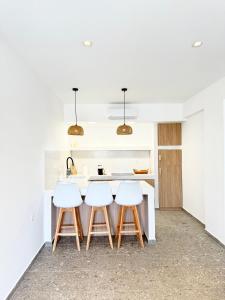 a kitchen with white counters and white counter stools at Sakellis Home 2- Steps to Beach & Town in Kardamaina