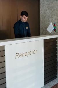 un hombre está parado detrás de una recepción en City Park Inn Baku, en Baku