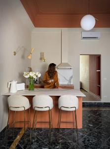 a woman sitting at a kitchen counter with three stools at Academia Apulian Suites - Marsia's Apartment in Mola di Bari