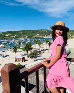 a woman in a pink dress standing on a balcony with a beach at Vista mar 1 in Arraial do Cabo