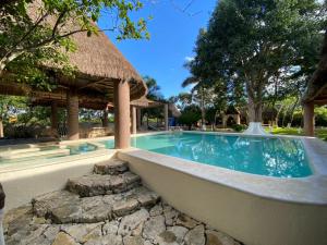 a swimming pool with a thatch roof and a resort at Hotel la Caprichozza in Conkal