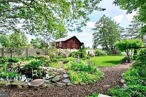 a garden with a creek and a barn at Historic Main Street Getaway 