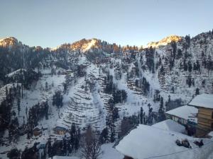 a mountain covered in snow with houses and trees at Boom shiva camps in Mandi