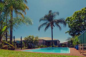 a swimming pool with palm trees in front of a building at Balan Village Motel in Nowra