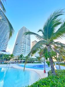 a palm tree next to a swimming pool with buildings at Soleil La Vie at Azure North Resort Residences in Lagundi