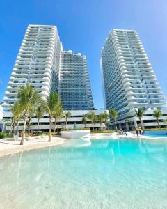 two tall buildings with palm trees in front of a swimming pool at Soleil La Vie at Azure North Resort Residences in Lagundi