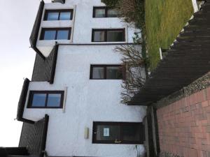 a white building with black windows next to a brick wall at Greannan Upper Self Catering Apartment in Blackwaterfoot +2 photos