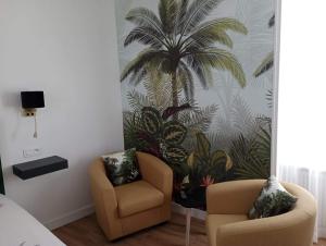 a bedroom with two chairs and a palm tree mural at Gîte La cour des trois rois 2 in Villedieu-les-Poêles
