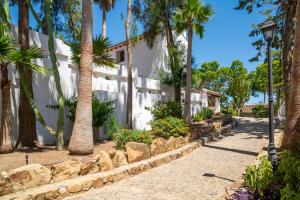 a white building with palm trees and a sidewalk at Málaga Sierra de las Nieves by Real Spain Hotels Adults Recommended in Casarabonela