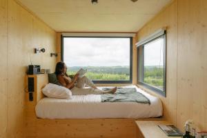 a woman sitting on a bed in a room with a window at Parcel Tiny House Couronneau près du Périgord in Ligueux