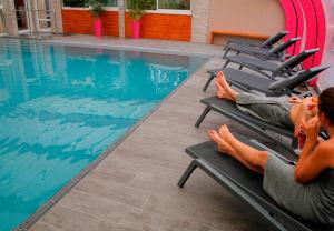 two people sitting on lounge chairs next to a swimming pool at Hotel & Spa Gil de France Cap d'Agde in Cap d'Agde