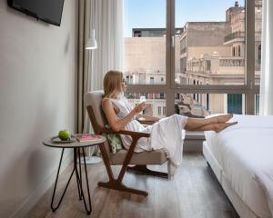 a woman sitting in a chair in a hotel room with a window at Casual Kubic Athens by Casual Hoteles in Athens