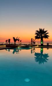 a pool with palm trees in front of a sunset at Pachia Ammos Falasarna in Falasarna