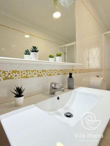 a bathroom with a large white sink and plants at Vila Maria Beach Apartments in Pataias +23 photos