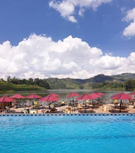 uma piscina com guarda-sóis vermelhos, mesas e água em Bunyonyi Safaris Resort em Kabale