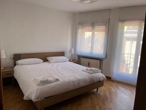 a bedroom with a bed with white sheets and two windows at Appartamento Sirio in Asiago