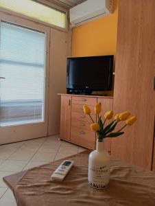 a vase of yellow flowers on a table with a television at Infinity Beach Germering in Balatonfüred