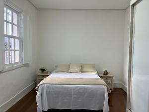 a white bedroom with a bed and two windows at Casa Zara in Diamantina