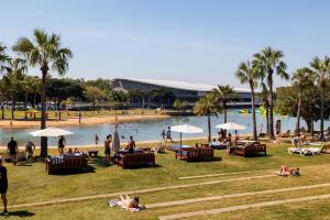 a group of people sitting on the grass near a pool at Delightful Waterfront Lagoon Views & Restaurants in Darwin
