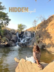 a young girl sitting on a rock by a waterfall at Whereabout Hostel Udaipur in Udaipur