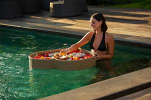 a woman in a swimming pool with a tray of food at The Artini Dijiwa Ubud in Ubud