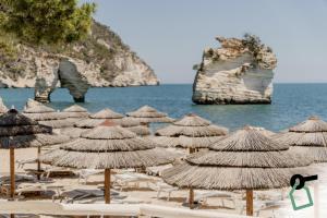 a group of straw umbrellas and chairs on a beach at HOTIDAY Room Collection - Mattinata Faraglioni in Mattinata
