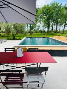 a red table and chairs with an umbrella next to a swimming pool at La Casa M-maison idéale pour groupes familles amis 12 personnes au calme avec piscine in Sainte-Hélène