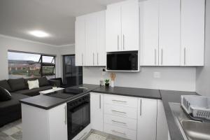 a kitchen with white cabinets and a living room at Meraki - Greek style beach house in Boggoms Bay in Boggomsbaai