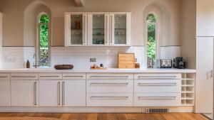 a kitchen with white cabinets and two windows at The Old Chapel in Painswick