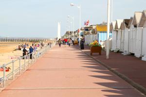 mensen lopen over een stoep naast een strand bij Maison Studios & Appartements Les 4 Vents in Luc-sur-Mer