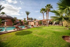 a lawn with benches and palm trees next to a swimming pool at Domaine Marradise in Marrakesh