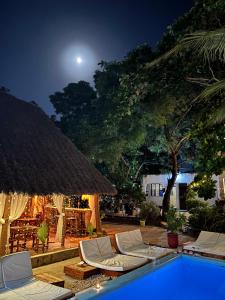 a pool with chaise lounge chairs and a thatch roof at Kilimanjaro in Nungwi