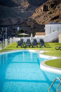 a swimming pool with chairs and a mountain in the background at Apartamentos Halley in Puerto Rico de Gran Canaria