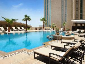 Una piscina en un hotel con sillas y palmeras. en Sofitel Abu Dhabi Corniche, en Abu Dabi