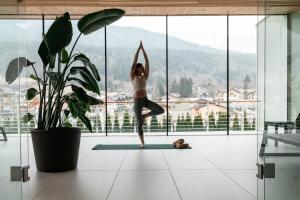 uma mulher fazendo ioga em uma sala com janela em Corona Dolomites Hotel em Andalo